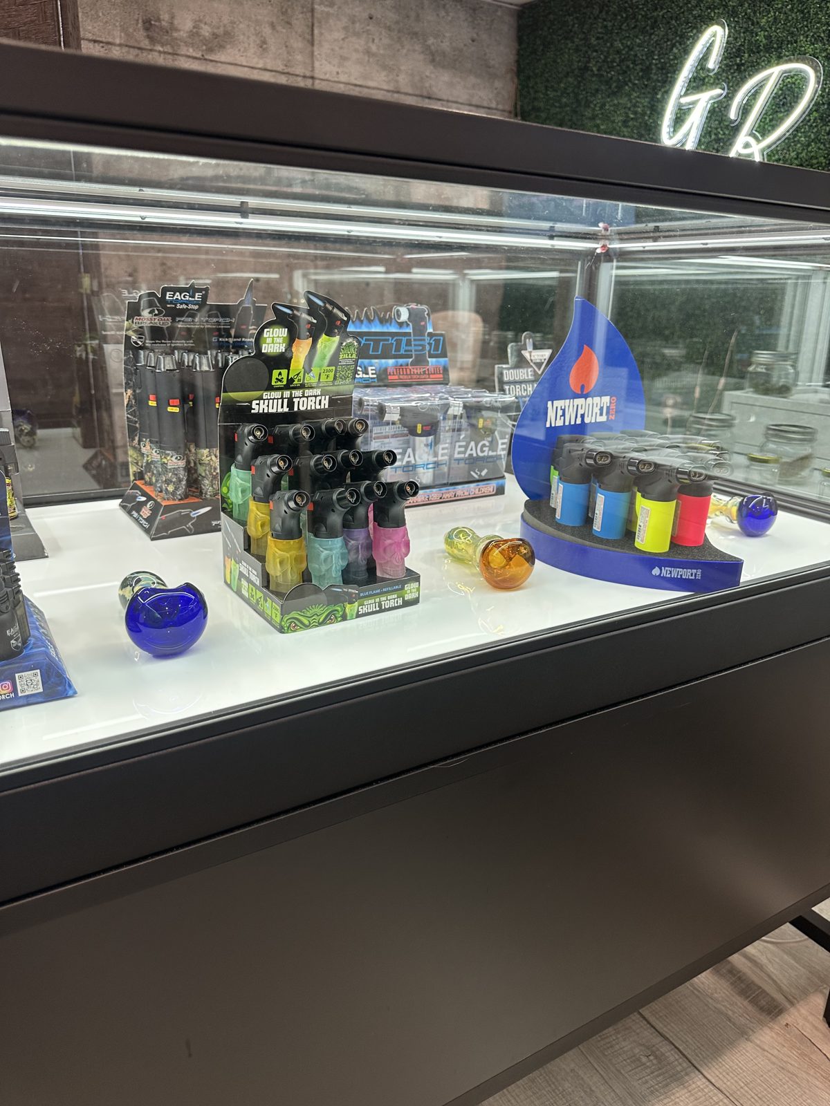 The accessories case at Grass Roots — glass, grinders and gear under the GR neon